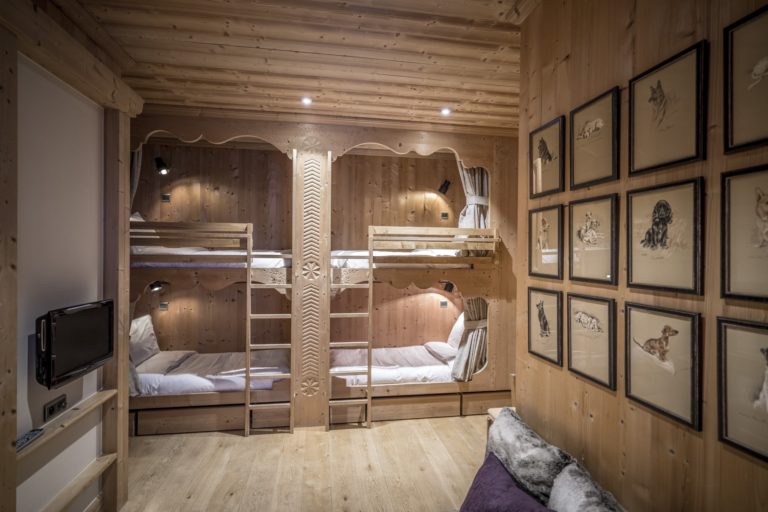 Chambre en bois avec deux lits superposés et des illustrations encadrées sur les murs.